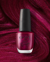 OPI nail polish bottle in the shade Big Sagittarius Energy, a deep shimmery magenta nail lacquer, standing upright against a swirling glittery berry-red background that matches the polish color.