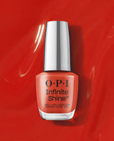 OPI Infinite Shine Full of Glambition coral-orange gel-like lacquer bottle standing on a glossy red polish background, a vibrant pick for fall nail colors.