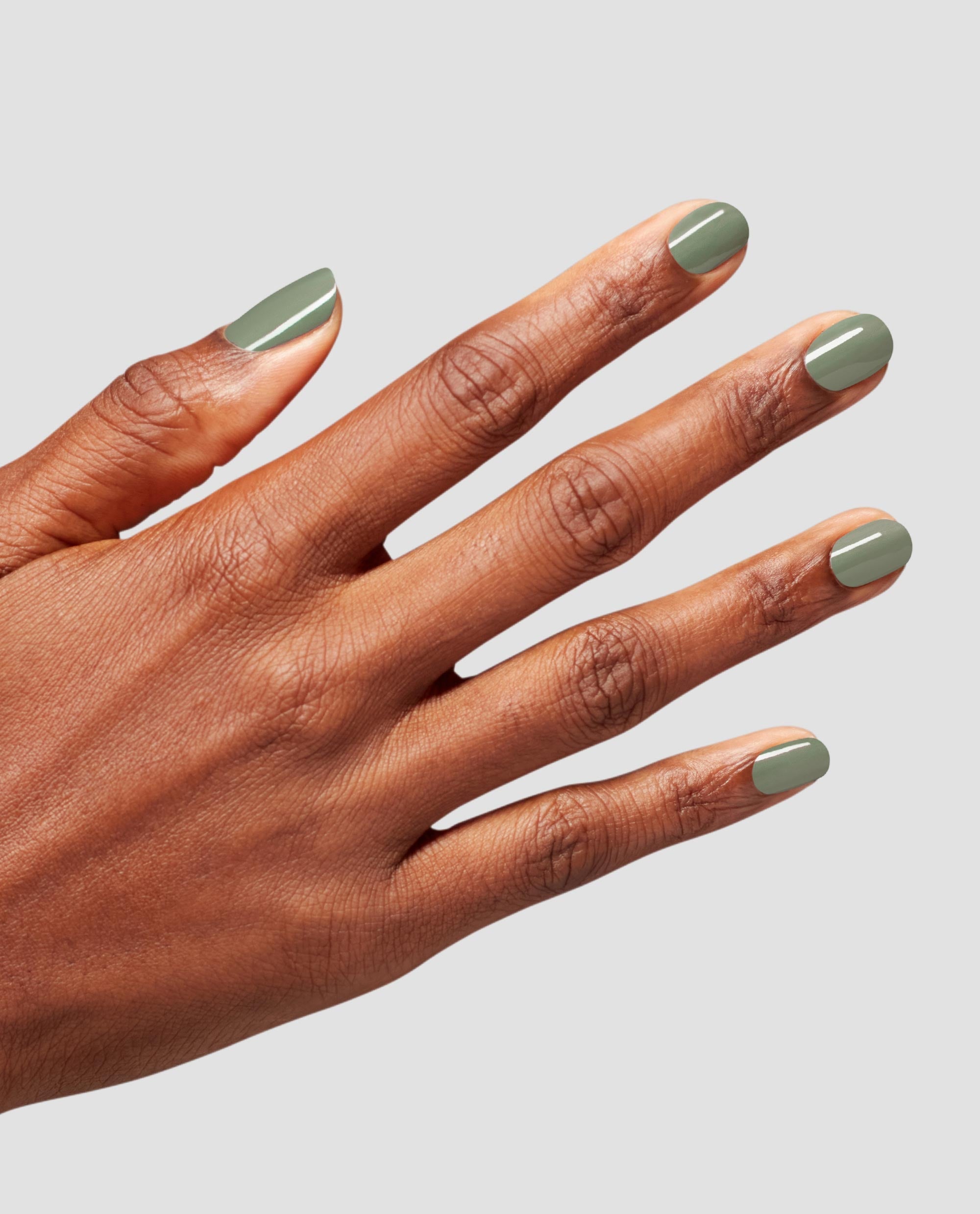 Short, rounded nails painted olive-sage with Cargo All Out nail lacquer, hand splayed to showcase a glossy, even coat against a clean light gray background, highlighting an earthy, on-trend choice for fall nail colors.