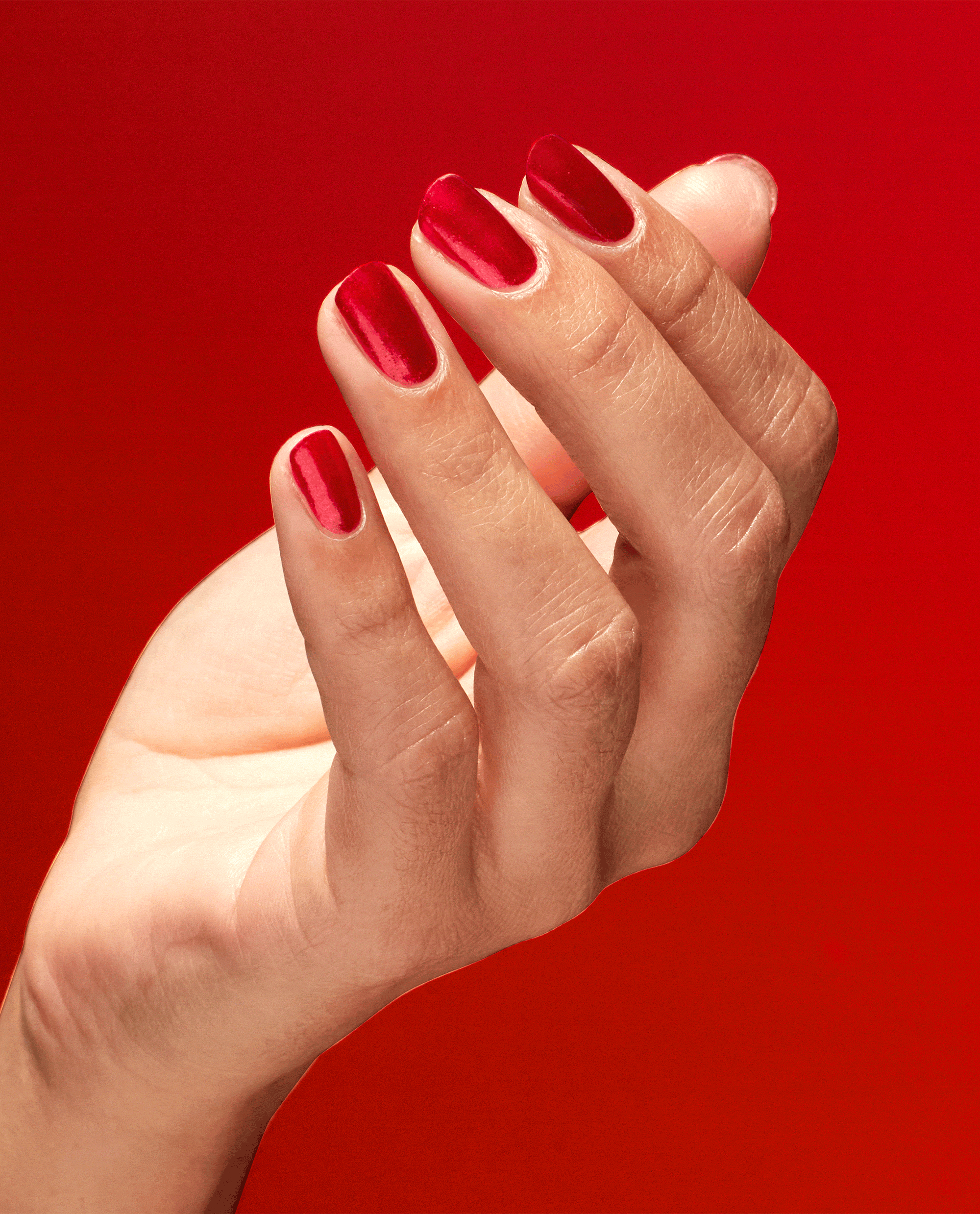 Hand tilting to showcase glossy red nails painted with Kiss My Aries OPI nail polish nail lacquer against a bold red background, highlighting the smooth, vibrant salon-quality finish for a fiery manicure look.