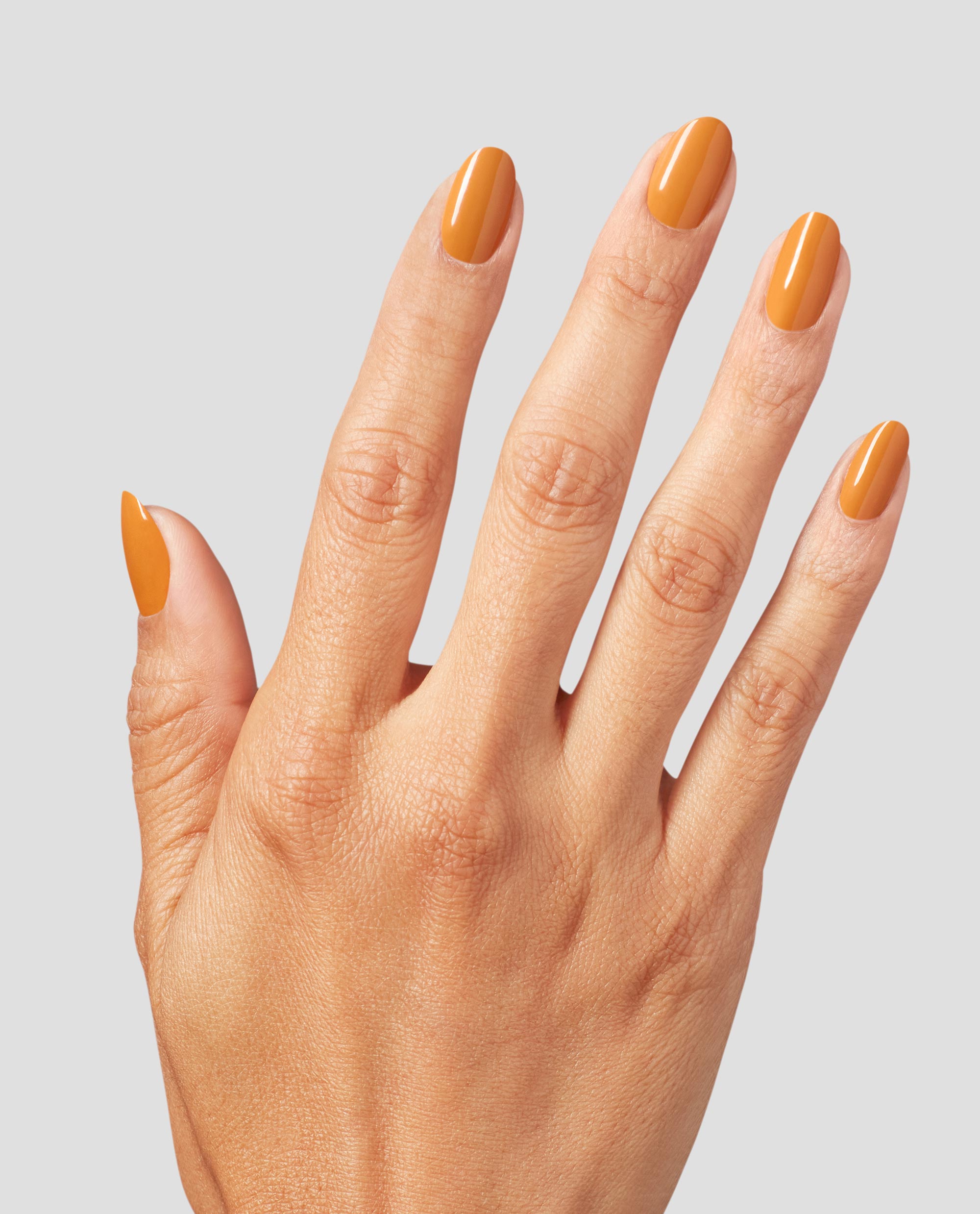 Hand with neatly manicured nails painted in Penny Loafer Lane, a warm caramel orange OPI nail polish shade, shown against a light gray background to highlight the glossy nail lacquer color and smooth finish.