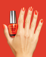 OPI Infinite Shine Shock Em Orange gel-like lacquer bottle held beside a hand with glossy orange shimmer nails on a bold red background, showcasing a trending bright manicure shade.