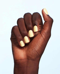 Hand displaying OPI Blinded by the Ring Light yellow nail lacquer on short, glossy rounded nails against a pale blue background.