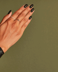 Hand with medium skin tone showing oval nails painted in OPI nail polish shade “Things I’ve Seen in Aber-green,” a deep glossy green nail lacquer, against an olive background with delicate gold rings highlighting the manicure.